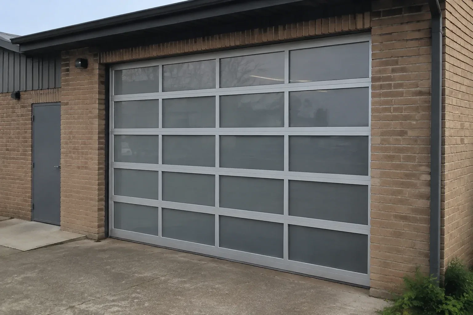 Closed glazed sectional door in a grey metal frame at a brick workshop. — Full-View Glass Garage Door Installation, Mississauga