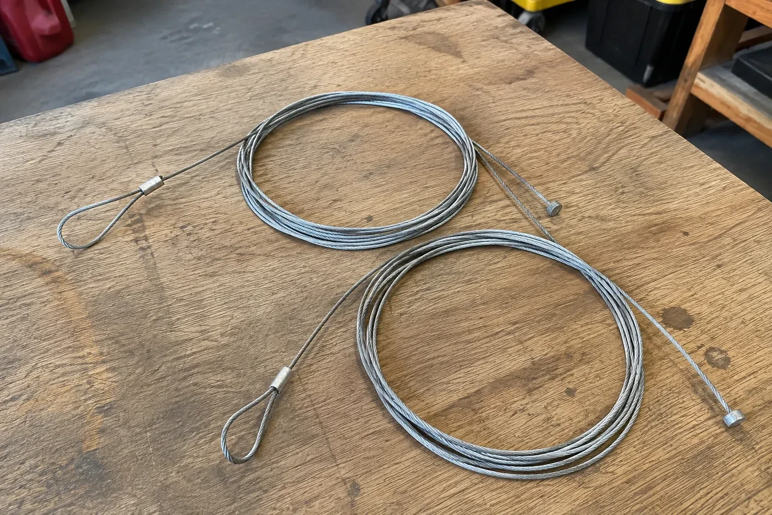 Two coiled steel cables with loop and stop ends on a workbench. — Garage Door Cable Replacement, Mississauga