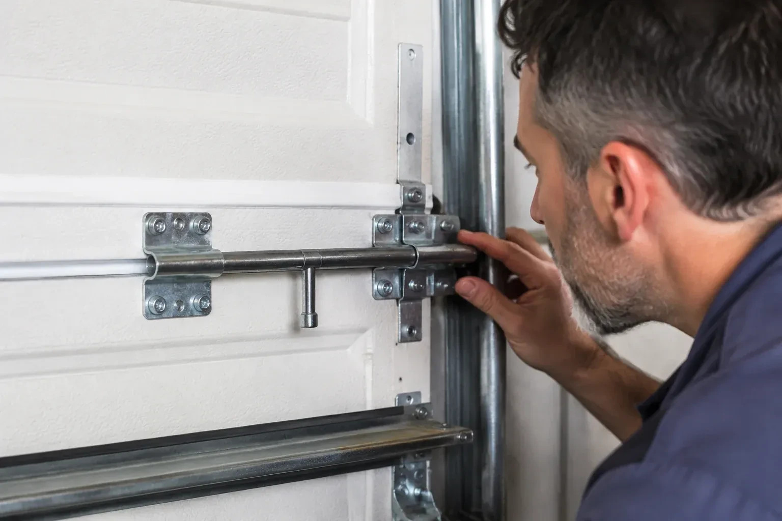 Person leaning close to a white paneled door, one hand on a metal slide-bolt bar mounted across the panel. — Garage Door Manual Lock Repair, Mississauga